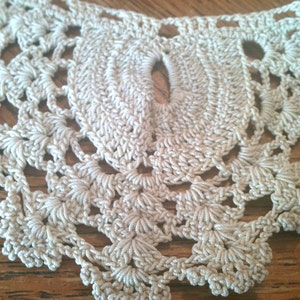 May include: Close-up of a cream-colored crocheted lace doily with a delicate floral pattern.