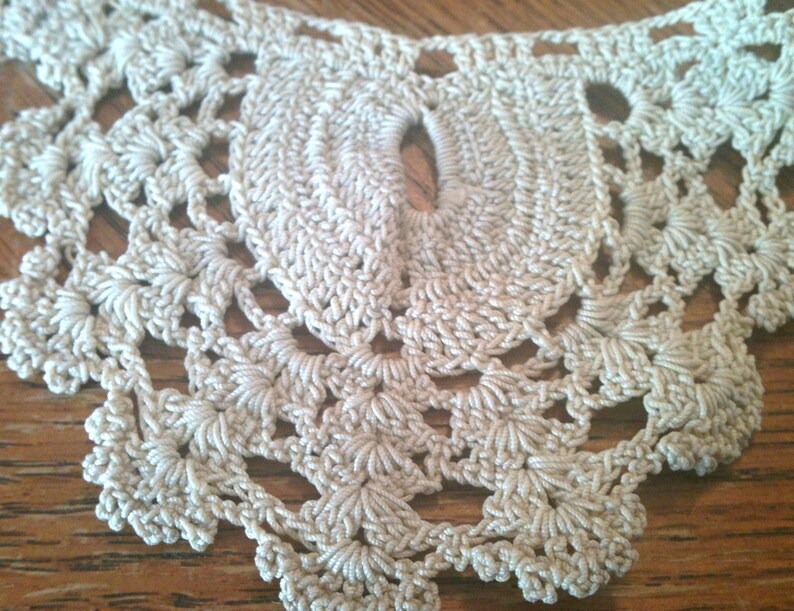 May include: Close-up of a cream-colored crocheted lace doily with a delicate floral pattern.