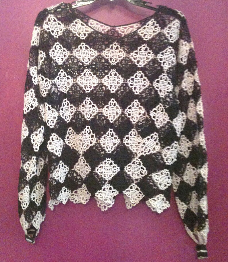 May include: Black and white crochet top with a scalloped hem and long sleeves.
