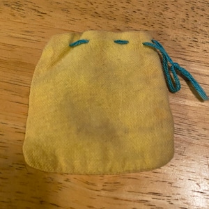 May include: A small yellow drawstring bag with blue stitching and a blue drawstring. The bag is made of a soft, velvety material.
