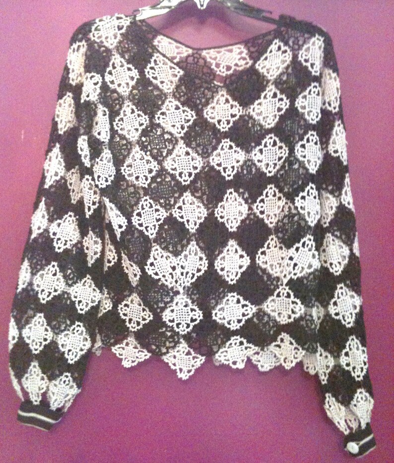 May include: Black and white crochet top with a scalloped hem and long sleeves. The sleeves have a black and white striped cuff.