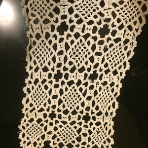 May include: A white crocheted lace doily with a delicate pattern of squares and diamonds.