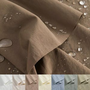 Pode incluir: Um tecido castanho com acabamento repelente à água, apresentando numerosas gotas de água transparentes na superfície. O material é mostrado em dobras, destacando a sua textura. É exibida uma paleta de cores branco, bege, castanho, creme, azul, verde e castanho-claro.