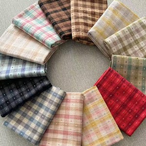 May include: A circular arrangement of twelve folded fabric swatches, each featuring a distinct plaid or checkered pattern with small white dots at the intersections. The colors include shades of red, blue, yellow, brown, black, green, and pink.