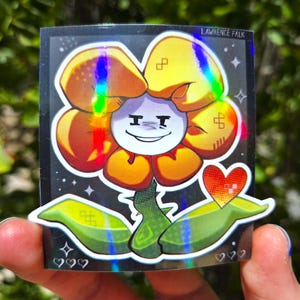 May include: A rectangular holographic sticker featuring a stylized yellow flower character with a white face, a smug expression, and green leaves. The design includes a small orange heart, stars, and the text LAWRENCE FALK at the top right corner.