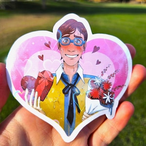 May include: A heart-shaped sticker featuring a cartoon illustration of a person with brown hair and blue glasses, blushing and sweating. The person wears a yellow shirt with a black tie, holding a red heart-shaped box and a bouquet of red and white flowers.
