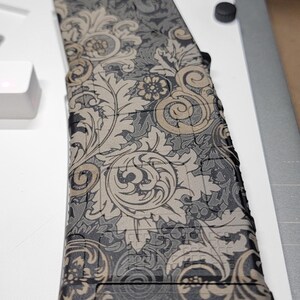 May include: A rectangular magazine featuring a detailed black and tan damask floral pattern. The surface displays intricate swirling leaves and flower motifs covering the entire exterior, with a textured grid pattern visible beneath the print.