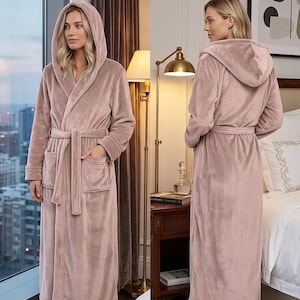 May include: A dusty rose, full-length plush bathrobe featuring a hood, long sleeves, two front patch pockets, and a matching tie belt. The robe is shown from both the front and the back, displaying a soft, velvety texture and a relaxed fit.