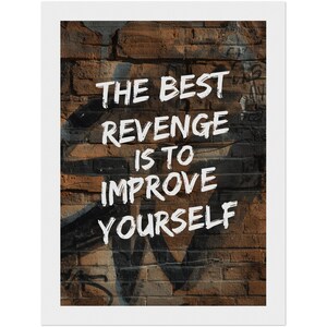 Op de afbeelding: Een ingelijste wandkunstprint met een witte tekstoverlay die luidt THE BEST REVENGE IS TO IMPROVE YOURSELF. De achtergrond toont een verweerde bruine bakstenen muur met donkergrijze graffitimarkeringen en een witte randlijst.
