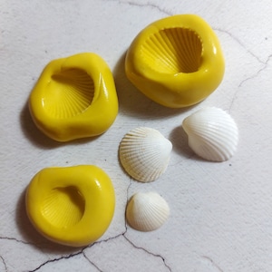 May include: Four yellow silicone moulds shaped like seashells, with four white seashells next to them.