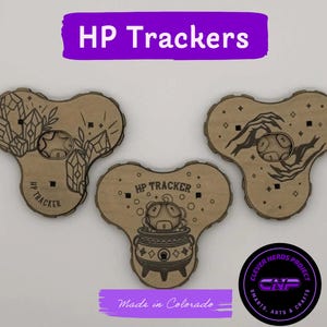 May include: Three light brown wooden HP tracker boards with a clover-like shape. Each board features a central circular cutout for a die, engraved illustrations of crystals, hands, or a cauldron, and the text HP TRACKER. A logo reads CLEVER NERDS PROJECT.