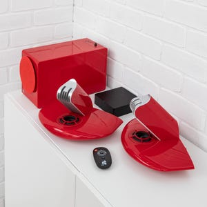 May include: A glossy red audio system consisting of a rectangular subwoofer, two uniquely shaped speakers with silver accents, a black square control unit, and a small black remote control with a red power button and white navigation icons.