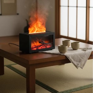 Puede incluir: Una chimenea eléctrica rectangular negra con frente de cristal que muestra brasas y leños rojos brillantes. Un efecto de llama naranja realista se eleva desde la parte superior. El dispositivo está sobre una mesa de madera junto a tres tazas.