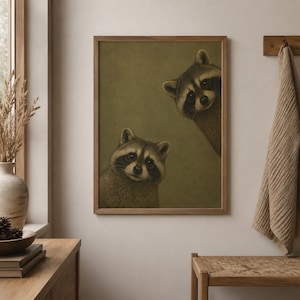 Puede incluir: Una impresión de arte mural rectangular en un marco de madera que muestra dos mapaches sobre un fondo verde oliva apagado. Un mapache está situado en la parte inferior izquierda, mientras que el otro asoma desde la esquina superior derecha, ambos con antifaces oscuros.