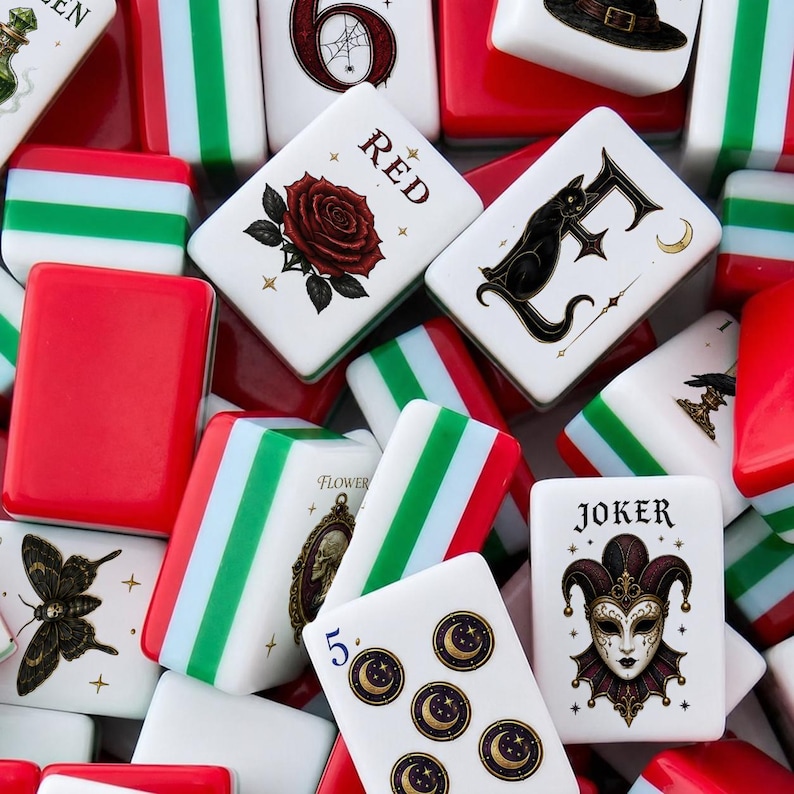 May include: A collection of rectangular mahjong tiles featuring white faces with various illustrations including a red rose, a black cat, a joker mask, a moth, and moon symbols. Some tiles display the text RED, FLOWER, and JOKER with red and green sides.