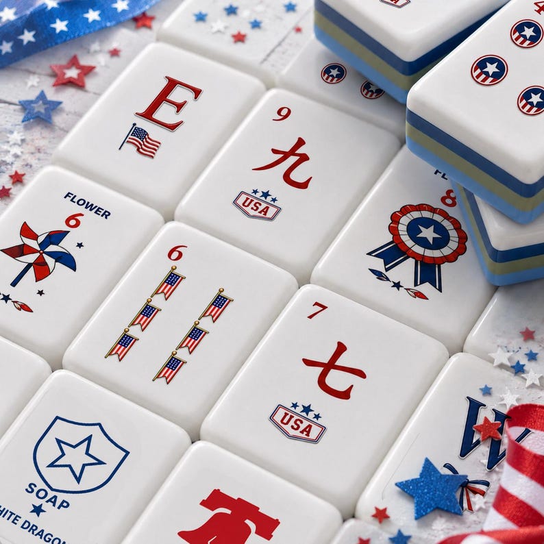 Puede incluir: Un conjunto de fichas de mahjong rectangulares blancas con gr&aacute;ficos patri&oacute;ticos en rojo, blanco y azul, incluyendo banderas estadounidenses, estrellas, molinillos y escarapelas. Algunas fichas muestran el texto USA, Flower o Soap junto a n&uacute;meros.