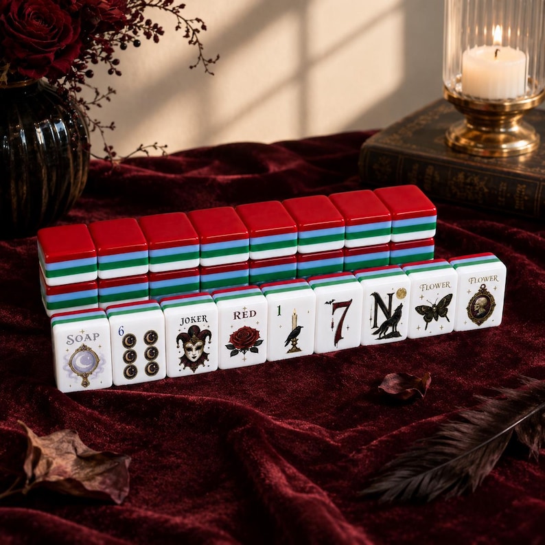 May include: A set of rectangular mahjong tiles with red, green, and blue layered edges. The front faces feature white surfaces with black and colored illustrations including a mirror, a joker, a rose, a raven, a wolf, a moth, and a skull.