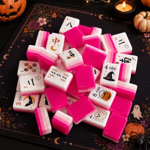 May include: A collection of rectangular Mahjong tiles featuring a pink and white gradient design. Several tiles display Halloween-themed graphics including ghosts, pumpkins, witch hats, and bats, alongside traditional numerical and character symbols.