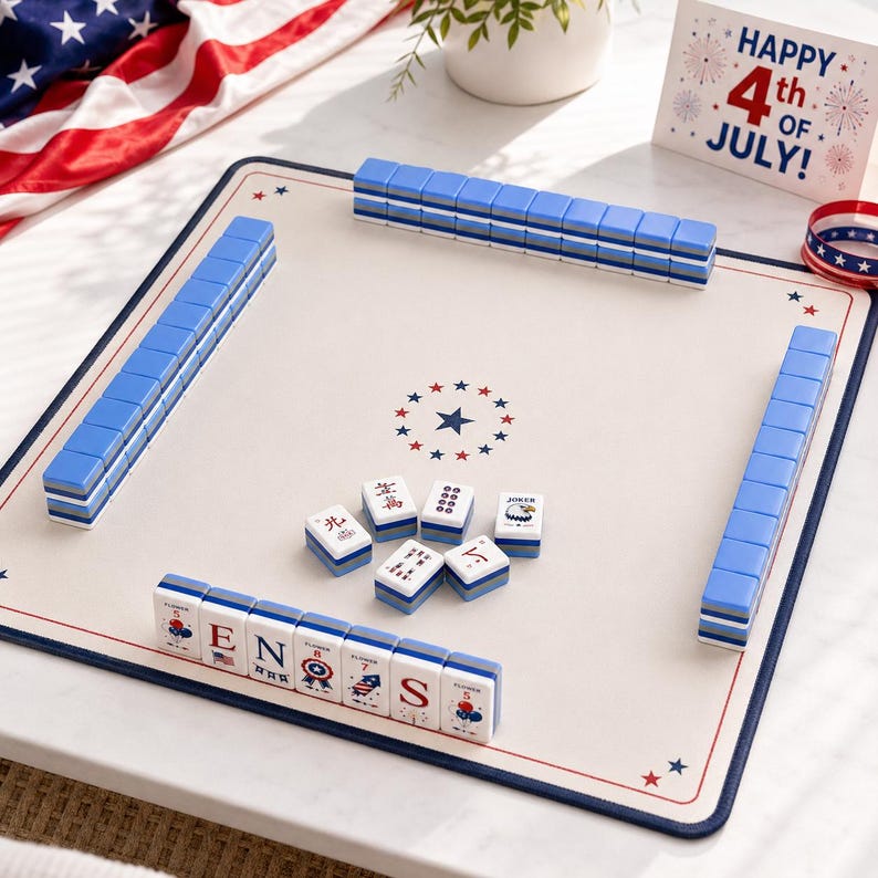 Puede incluir: Un juego de Mahjong con un tapete de color crema que presenta una estrella central y detalles en rojo, blanco y azul. Las fichas est&aacute;n dispuestas en filas con el reverso azul, mientras que varias fichas muestran gr&aacute;ficos patri&oacute;ticos.
