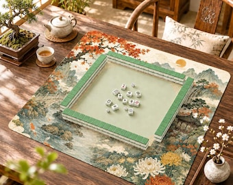 Könnte beinhalten: Eine quadratische Mahjong-Matte mit einem detaillierten Landschaftsdruck aus Bergen, Bäumen und Blumen. Die Matte hat einen erhöhten grünen Rand, der eine quadratische Spielfläche bildet, mit mehreren weißen Mahjong-Steinen in der Mitte.