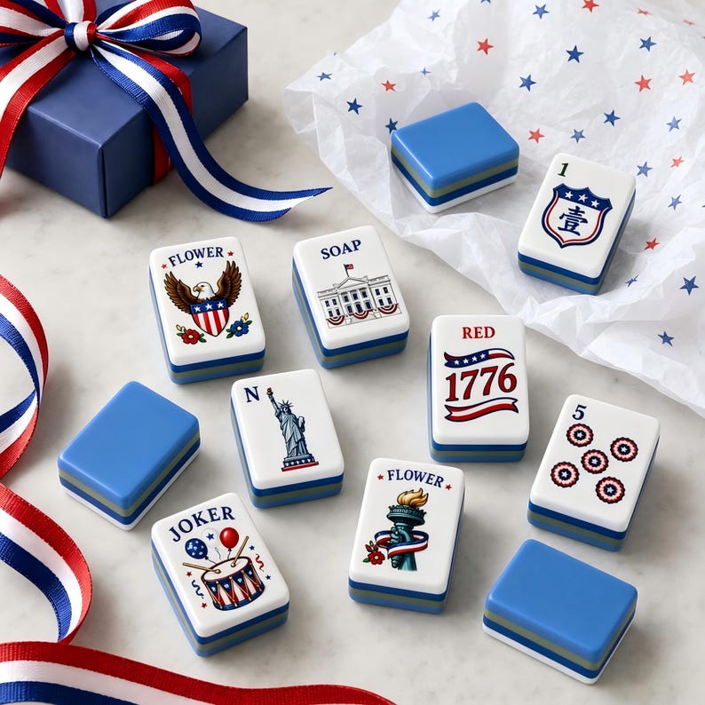 May include: A set of rectangular mahjong tiles featuring patriotic American-themed illustrations, including the Statue of Liberty, the White House, an eagle, and the text 1776, alongside blue gift boxes and red, white, and blue striped ribbons.