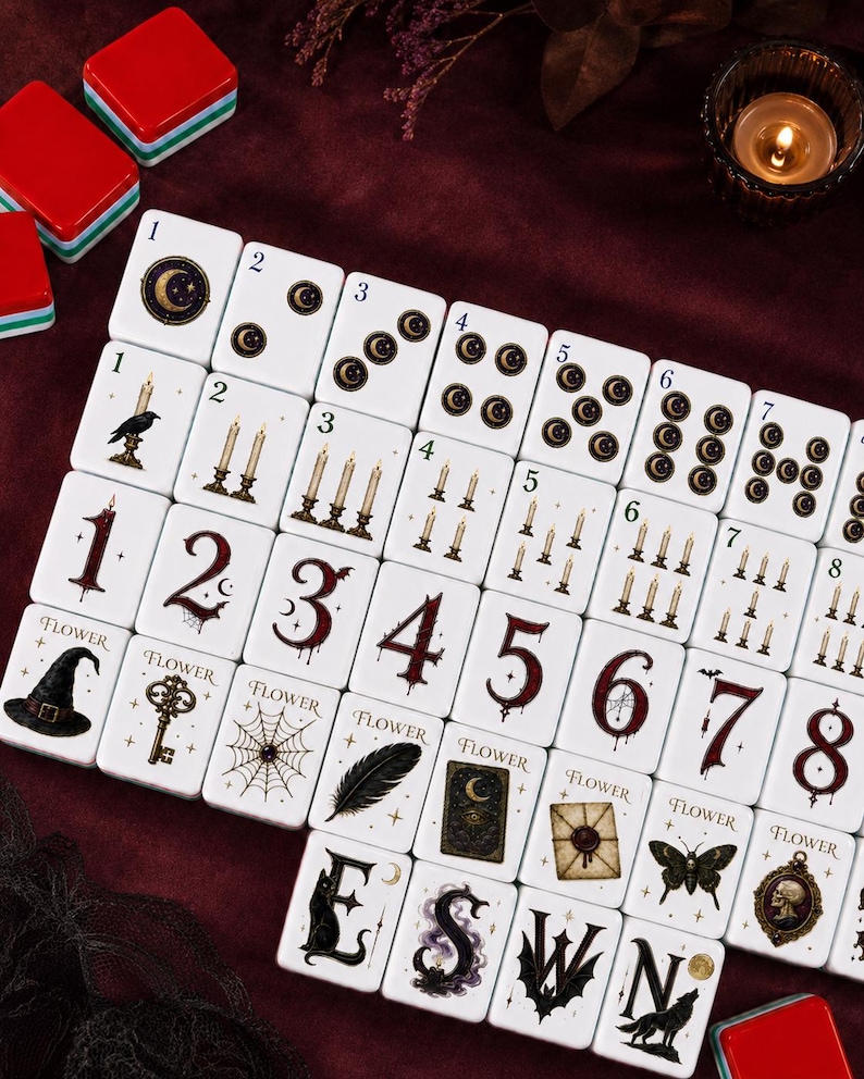 May include: A set of white rectangular mahjong tiles featuring dark, gothic-themed illustrations including crescent moons, lit candles, spiderwebs, keys, witch hats, feathers, moths, and skulls, with numbers and letters printed in a stylized red or black font.