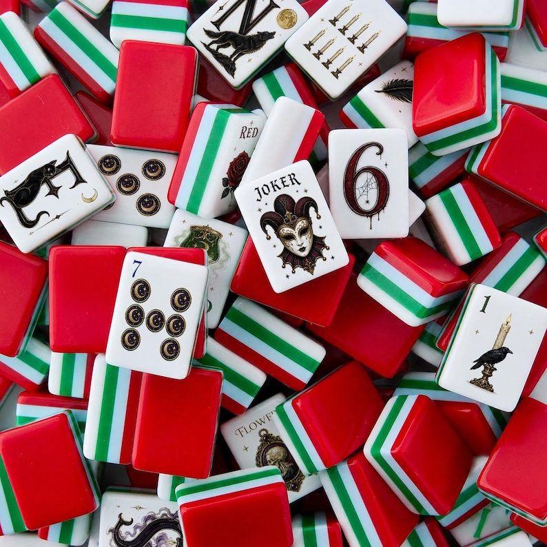 May include: A collection of mahjong tiles featuring red, white, and green striped backs and white faces with various illustrations including a jester joker, a number six, a number seven with moon symbols, a raven with a candle, and a wolf.