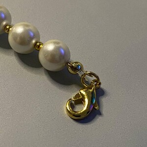 May include: A necklace featuring a series of round, white, lustrous beads separated by small, polished gold-tone metal spacers. The strand terminates with a gold-tone metal lobster claw clasp attached to a small jump ring, providing a secure closure.