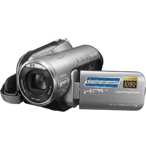 May include: A silver Sony Handycam HDV camcorder featuring a Carl Zeiss Vario-Sonnar lens, CMOS sensor, and a flip-out LCD screen. The screen displays text including Full HD 1080, HDV, and Clear Photo LCD plus. A grey hand strap is attached.