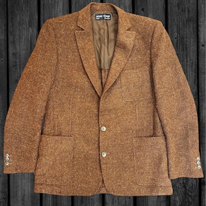 May include: A brown textured blazer with a speckled finish, featuring a notched lapel, two front buttons, three buttons on each cuff, two lower patch pockets, and one chest patch pocket. The interior label reads Andre Oliver Paris New York.