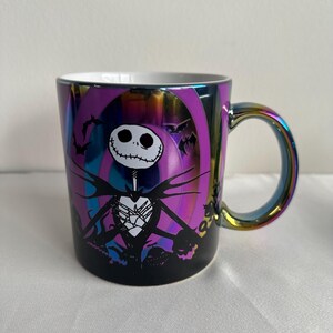 Pode incluir: Uma caneca de cer&acirc;mica com acabamento iridescente multicolorido apresentando um gr&aacute;fico de Jack Skellington de O Estranho Mundo de Jack. O design inclui uma silhueta preta do personagem contra um fundo circular roxo e azul.