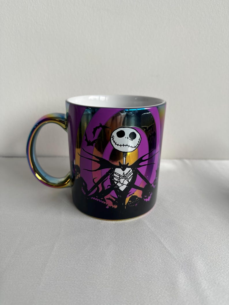 Pode incluir: Uma caneca de cer&acirc;mica com acabamento iridescente apresentando um gr&aacute;fico de um personagem esquel&eacute;tico em um terno risca de giz contra um fundo espiral roxo. O design inclui silhuetas pretas de morcegos e ab&oacute;boras, com interior e al&ccedil;a brancos.