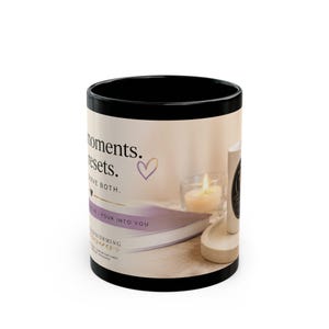 May include: A black ceramic mug featuring a printed design with the text 'moments. resets. DESERVE BOTH.' and 'BREATHE | POUR INTO YOU'. The graphic includes a lit candle in a glass holder, a book, and a small heart icon in shades of purple and cream.