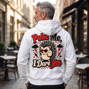 Puede incluir: Una sudadera con capucha blanca que presenta un gráfico en la espalda de un erizo con gafas de sol en forma de corazón, levantando una mano en señal de alto, con el texto "Poke Me, I Dare You" en letras rojas y negras, rodeado de nubes y rayos.