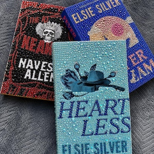 May include: Three hardcover books decorated with rhinestones. The left book is black and red with a skull graphic. The top book is blue with gold text reading ELSIE SILVER and FEVER. The front book is light blue with a guitar and hat graphic and text reading HEARTLESS ELSIE SILVER.