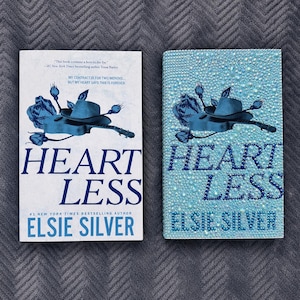 May include: Two copies of the book Heartless by Elsie Silver. The left copy has a white cover with a blue illustration of a hat, guitar, and roses. The right copy is covered in light blue rhinestones, featuring the same blue graphic design.