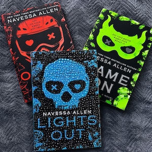 May include: Three books by Navessa Allen. The top left book is red and black with a helmet graphic and text reading Get On Your Knees And Prey. The top right book is green and black with a mask graphic and text reading Put Your Mouth Where Your Money Is. The bottom book is blue and black with a skull graphic and the text Lights Out.