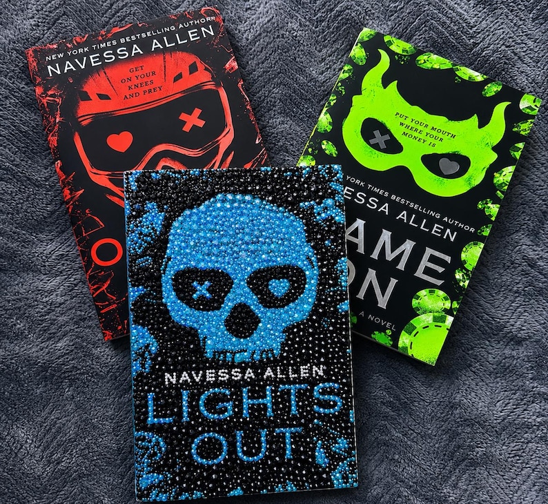 May include: Three books by Navessa Allen. The top left book is red and black with a helmet graphic and text reading Get On Your Knees And Prey. The top right book is green and black with a mask graphic and text reading Put Your Mouth Where Your Money Is. The bottom book is blue and black with a skull graphic and the text Lights Out.