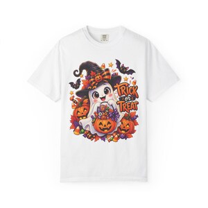 Puede incluir: Una camiseta blanca con un gráfico de un fantasma sonriente con sombrero de bruja, sosteniendo un cubo de calabaza lleno de dulces. El diseño incluye calabazas naranjas, hojas de otoño, murciélagos y el texto Trick or Treat en naranja y negro.