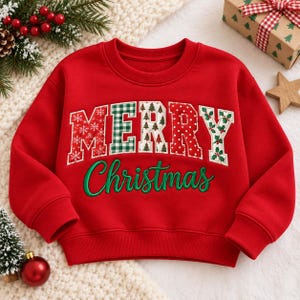 May include: A bright red long-sleeve sweatshirt featuring the word MERRY in large, multi-patterned block letters with various holiday prints, and the word Christmas embroidered in green cursive script across the center of the chest.