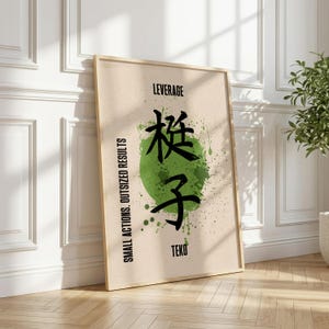 May include: A framed wall art print featuring a beige background with a subtle geometric pattern. A large green ink splatter circle sits in the center behind black Japanese kanji characters. The text reads LEVERAGE, TEKO, and SMALL ACTIONS. OUTSIZED RESULTS.