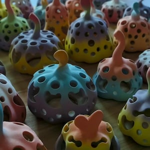 Puede incluir: Una colección de pequeños objetos decorativos con forma de calabaza y acabado en degradado. Cada pieza tiene un cuerpo hueco y redondeado con varios recortes circulares y en forma de corazón, y un tallo curvado en la parte superior.