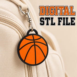 May include: A circular basketball-themed keychain featuring an orange surface with black lines, attached to a silver metal clasp. The text DIGITAL STL FILE is displayed in bold orange and black lettering above the keychain.