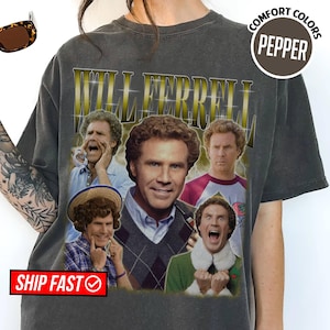 Op de afbeelding: Een antracietgrijs t-shirt met een grafische print van Will Ferrell in verschillende filmrollen. De tekst "WILL FERRELL" staat in grote gouden letters bovenaan. Het t-shirt heeft een vintage wassing, een ronde hals en korte mouwen.