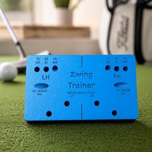 May include: A rectangular blue Zwing Trainer golf practice aid featuring printed text and circular cutouts. The surface displays labels including 72 DR, 60 6i, 48 SW, LH, RH, and 25 degree inside markings, designed for wedge impact training.