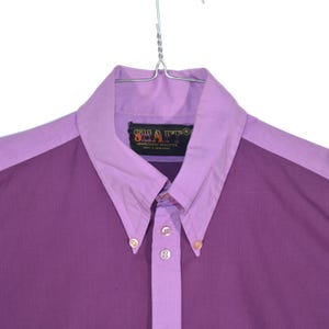 Könnte beinhalten: Ein lila und helllilafarbenes Hemd mit Knöpfen und einem kontrastierenden Kragen. Das Hemd hat ein Etikett mit der Aufschrift "SHARP" "SUPERIORLY STYLISTIC" "MADE IN TAIWAN".