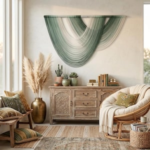 May include: A large wall hanging featuring layered green and white fiber strands draped in a curved, scalloped pattern. The piece is mounted on a horizontal rod and displays a gradient of sage and forest green tones transitioning into white.