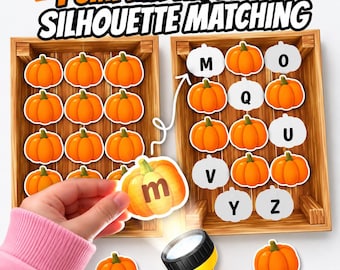 Op de afbeelding: Een Pumpkin Alphabet Silhouette Matching educatieve activiteit met twee houten kratten, oranje pompoenen en witte pompoensilhouetten met de letters M, Q, U, V, Y, Z. Een hand houdt een pompoen met de letter m bij een gele zaklamp.