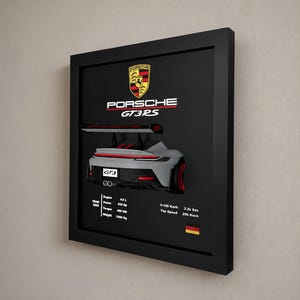 Könnte beinhalten: Ein gerahmtes Wandbild mit einer silbernen Porsche GT3RS in der Heckansicht. Der schwarze Hintergrund zeigt das Porsche-Logo und technische Daten: 4.0 L Motor, 525 PS, 465 Nm Drehmoment, 1500 kg Gewicht, 3.2s von 0-100 km/h und 296 km/h Höchstgeschwindigkeit.