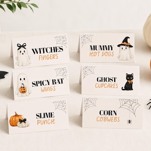 May include: Six white folded paper food labels with black and orange Halloween-themed text and illustrations. The cards feature graphics of ghosts, a black cat, pumpkins, and spiderwebs, with text reading Witches Fingers, Mummy Hot Dogs, Spicy Bat Wings, Ghost Cupcakes, Slime Punch, and Corn Cobwebs.